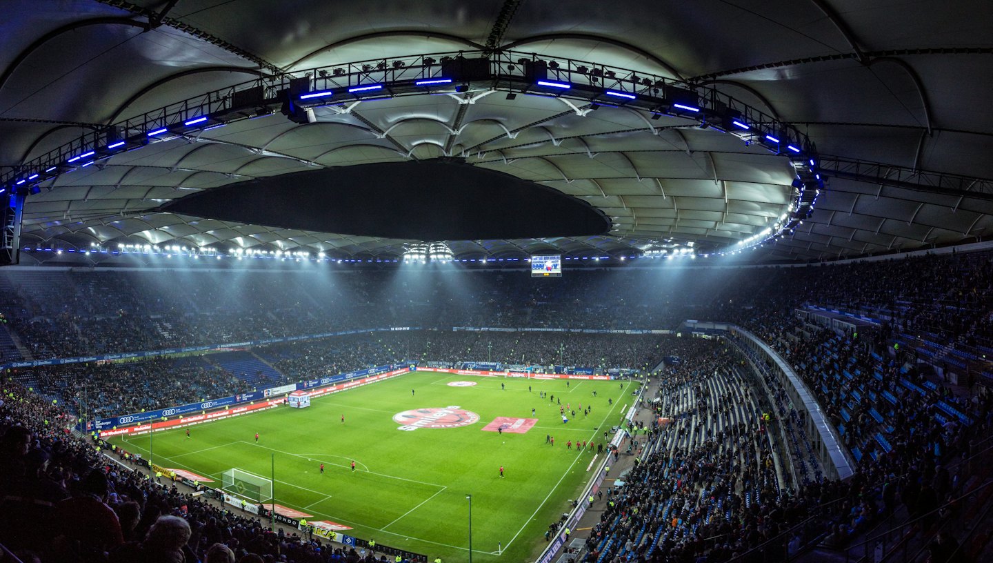 Estadio de fútbol moderno lleno de aficionados por la noche bajo luces brillantes.